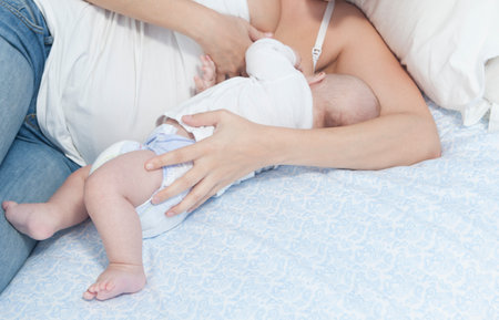 Young mother feeding breast her baby laying in her bedroom. Soft photoの写真素材
