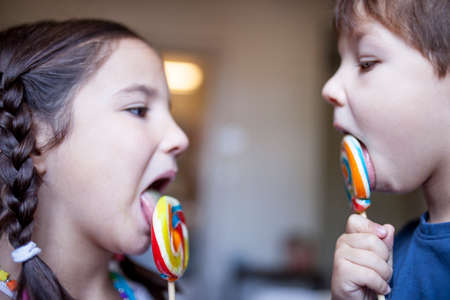 Two children licking a colorful big lollipop. Selective focus. Unhealthy food for children conceptの写真素材