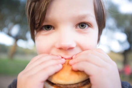 Little boy bites hamburger outdoors. closeupの写真素材