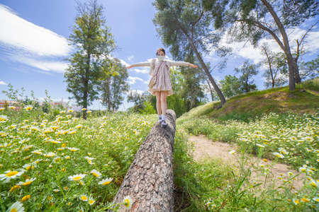 Little girl walking on a log in the middle of daisy field. She wears a facemask
