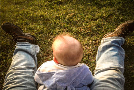 Baby boy sitting on grass between his fathers legs. Fathers taking care of babies concept