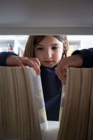 Young girl selecting books from library bookshelf. Children creativity and imagination concept.