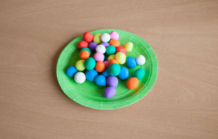Plastic plate full of colorful playdough balls. wood background