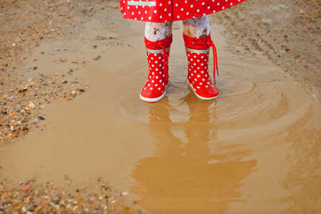 Detail of rainboots of a baby girl dressed with dotted raincoat in the puddlesの写真素材