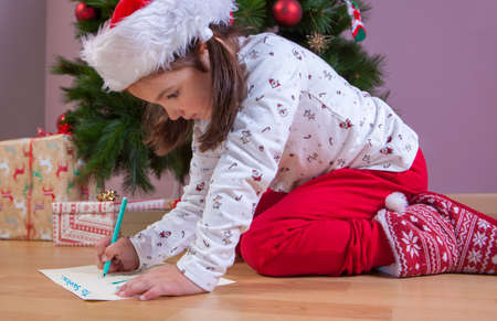 Little girl preparing The Santa Letter. She painting a sheet with header in English