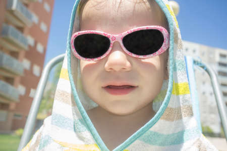 2 year old baby boy with hooded poncho towel after swimming. He is sitting over beach chairの写真素材