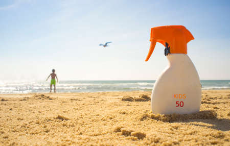 Sunblock cream with Sun Protection Factor or SPF 50 on beach sand. Child boy on background