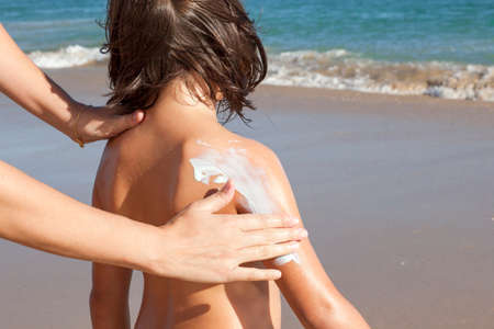 Mother applying sunblock cream to her daughter on arm. idyllic beach background