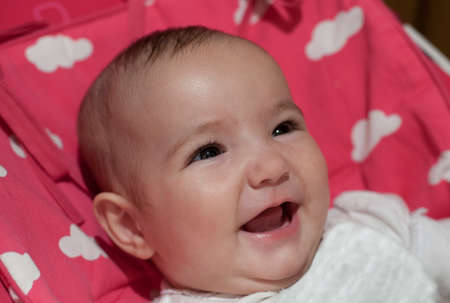 Laughing 3 months baby girl. She is reclined over pink padding blanket