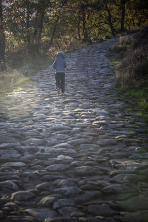 Child boy climbing alone a steep stone pavement path. Individual effort concept for childrenの写真素材