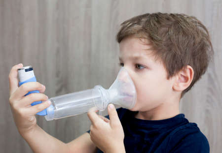 Child boy using medical spray for breath. Inhaler, spacer and mask. side view
