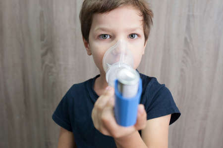 Child boy using medical spray for breath. Inhaler, spacer and mask. front view