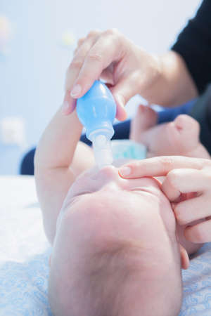 Mother using baby nasal aspirator. She is doing a mucus suction to three months baby boyの写真素材