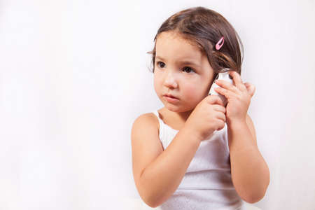 Little girl with ear talking electronic thermometer taking herself the temperature. Isolated over...