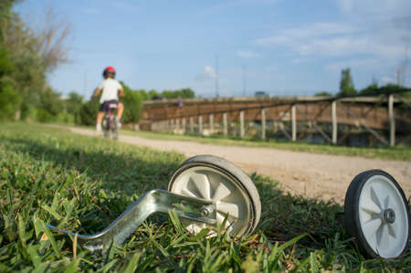 Additional wheels lying on the grass while a boy begins to ride without them. First day without...