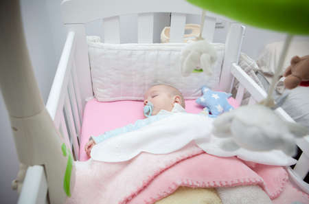 Sleeping four month baby boy lying in cot with mobile. overhead view