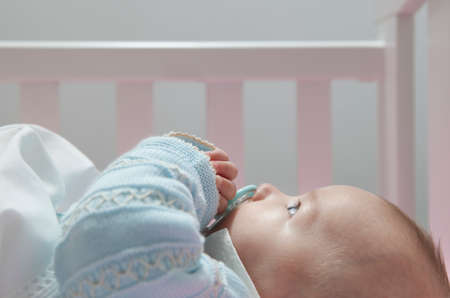 Awake four month baby boy lying in cot with pacifier. side view