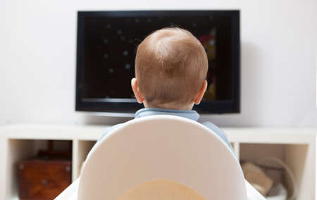 Baby boy watching cartoons on TV. He is sitting on his highchair. back viewの写真素材