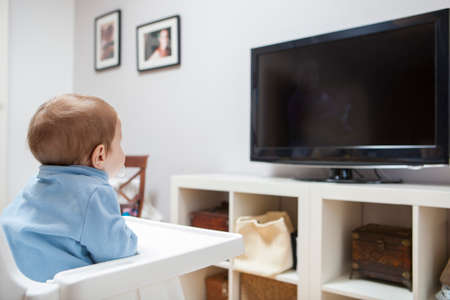 Baby boy watching TV. He is sitting on his highchairの写真素材