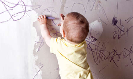 Baby boy drawing with wax crayon on plasterboard wall. He is with his back towardsの写真素材