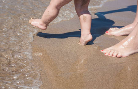 Mother and baby feet walking on sand beach for first time