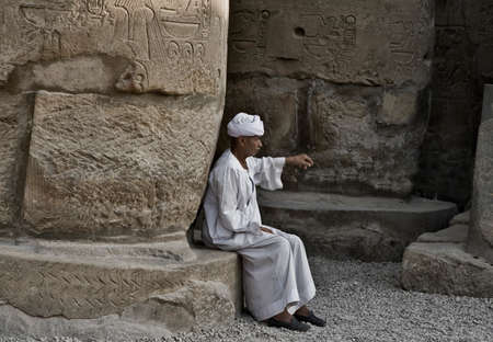 LUXOR, EGYPT - JULY 19: Old Egyptian beggar sitting on a base column of Luxor temple. On July 19, 2010 Luxor, Egyptのeditorial素材