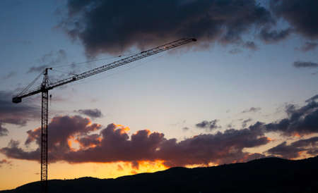 Construction crane silhouette over red sunset and hills. Real State on countryside conceptの写真素材