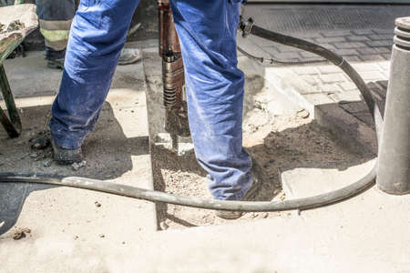Builder worker with pneumatic hammer drill equipment breaking sidewalk asphalt on street