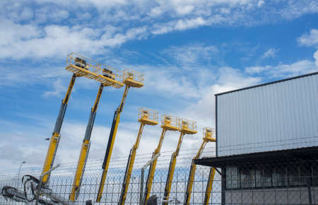 Telescopic Booms at industrial unit. Some platforms lifted over blue sky