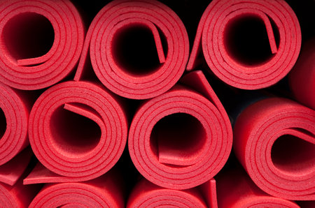 Lot of rolled up red foam fitness mats background. travel and sports