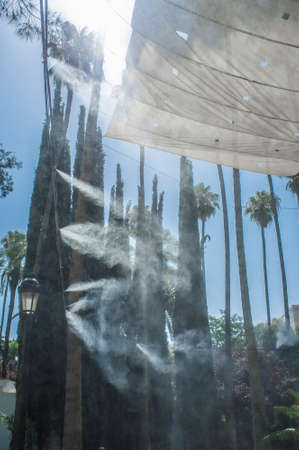 Awning and sprinklers splashing vaporized water at public park. Devices for cooling the hot summer temperature in Spain outdoorsの写真素材