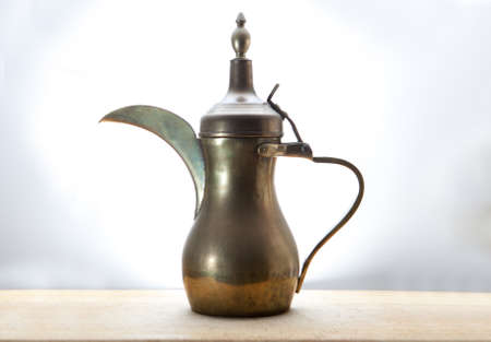 Old traditional arabic pitcher isolated over white background, placed on wooden surfaceの写真素材