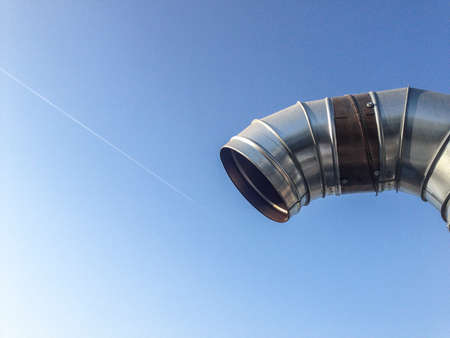Curved steel pipes as smoke stack over blue skyの写真素材