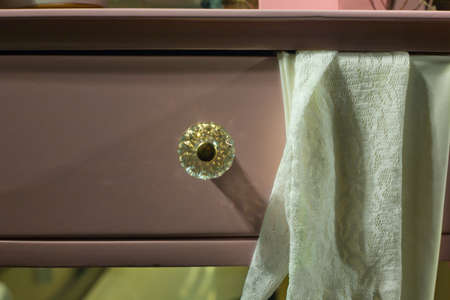 Pink drawer with shiny glass handle and piece of fabric on boudoir