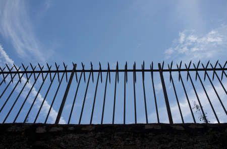 Wrought iron spiky fence placed on the top of a wall. blue cloudy skyの写真素材