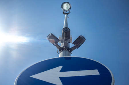 Three surveillance cameras attached on traffic signal pole with led spotlight on the top. Blue sky...
