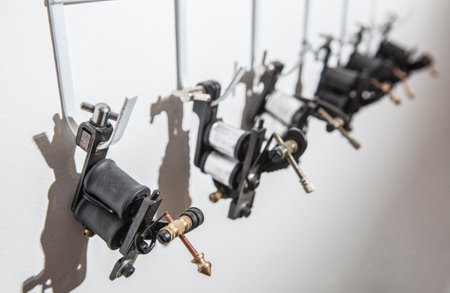 Tattoo coil ink machines hanging from hooks on white wall. closeupの写真素材