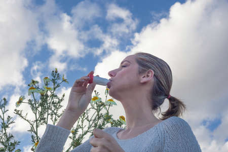 Young woman using inhaler to treat asthma allergic at flowers meadowの写真素材