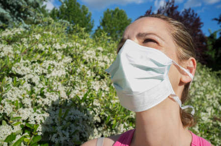 Young woman with protective mask at blooming park with half-closed eyes because of the strong sunの写真素材