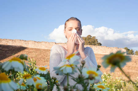 Young woman sneezing in a daisy flowers meadow. She is allergic to flowersの写真素材
