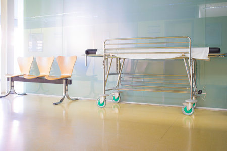 Interior of healthcare center hallway. Modern and gleaming environment with stretcher and wooden waiting chairsの写真素材