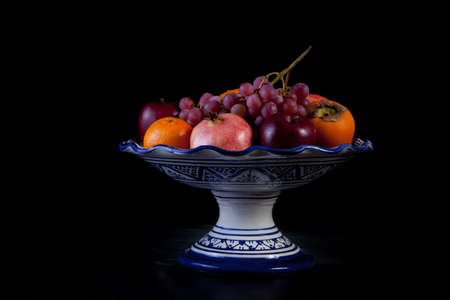 Ceramic fruit bowl with autumn fruits isolated over black backgroundの写真素材