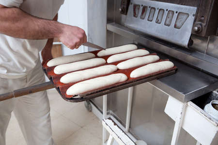 Baker making patterns on raw bread using a knife to shape the dough prior to baking. Manufacturing...