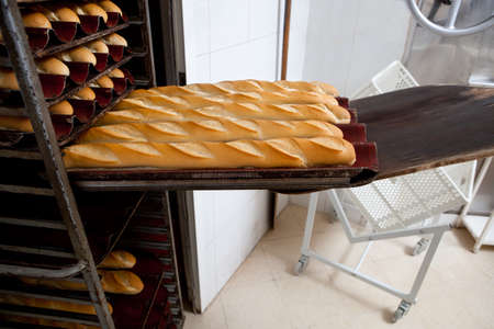 Putting fresh baked baguette bread into the rack. Manufacturing process of spanish bread