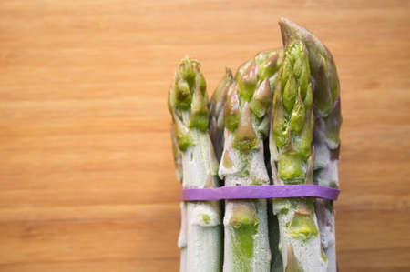 Bunch of frozen wild asparagus tied with rubber tape from ecological agriculture over wooden background. overhead shotの写真素材