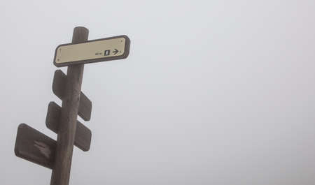 Wet rusty wooden pole with hiking tracks direction on thick fog. Torcal of Antequeraの写真素材