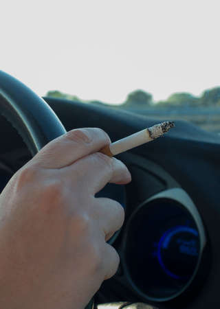 Woman smoking while she is driving. Cause of distracted driving accidents concept. Inside car viewの写真素材