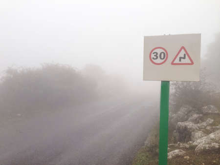 Metal pole with traffic signal advice danger signal of curves at mountain road in the fogの写真素材