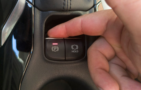Driver activating the electric parking brake of his car. Selective focus on button