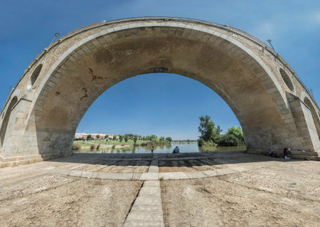 Fishermen sitting under Puente de Palmas arch, Badajoz, Spain. Extra wide angle viewの写真素材
